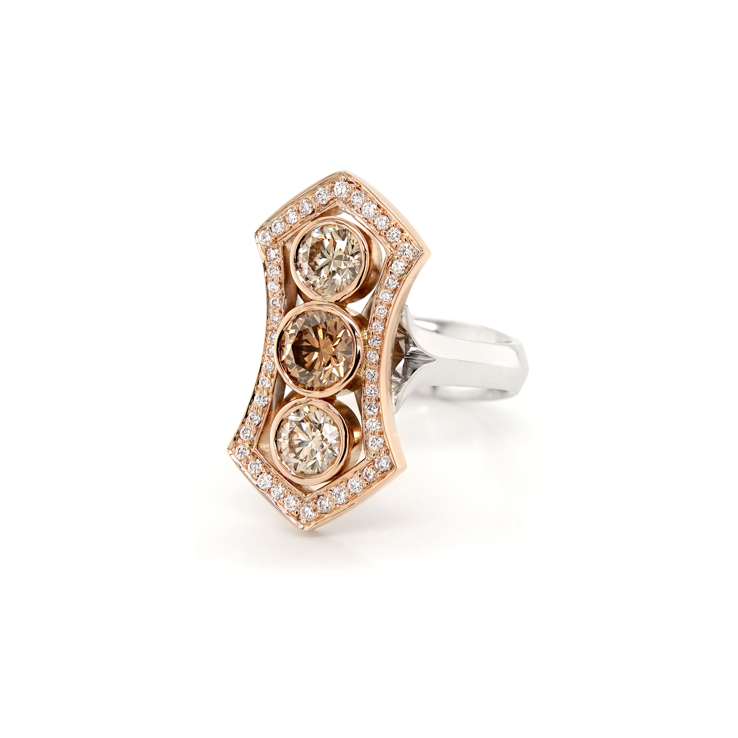 A dress ring. Three round brilliant cut Argyle champagne diamonds are bezel set in rose gold in a vertical formation, the centre stone being a darker colour than the outer two. The central three stones are surrounded by a decorative, shield like shaped halo of round brilliant cut diamonds grain set in rose gold. The white gold band features a knife edge, which splits and flares to meet the top of the undersetting.